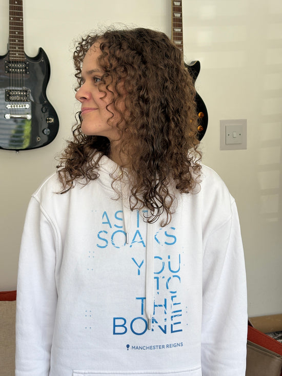 Person wearing a white hoodie with text, standing next to a guitar indoors.